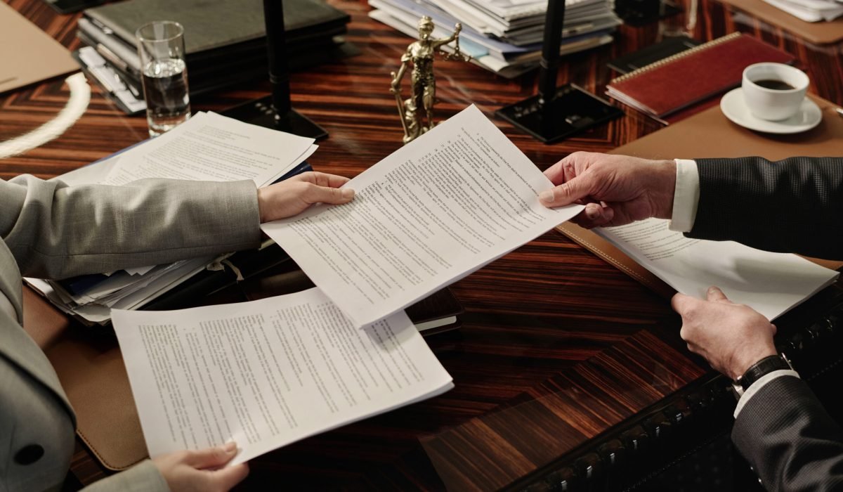 Closeup of hands of unrecognizable lawyers passing documents to each other over wooden desk