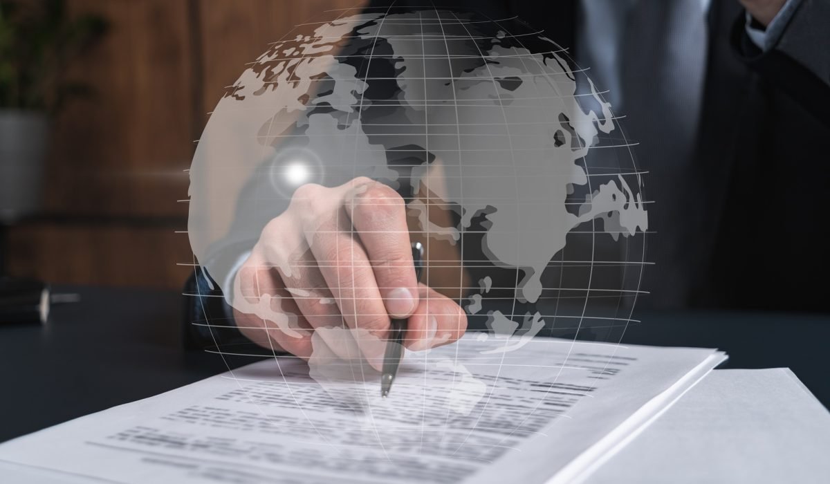 Businessman in suit signs contract. Double exposure with world map hologram. Man signing agreement international business concept.