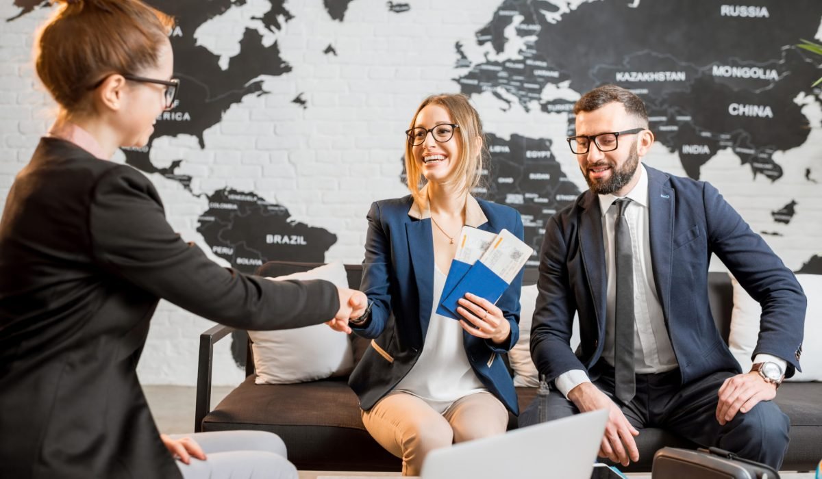 Young businesscouple choosing a trip with agent sitting at the travel agency office with world map on the background