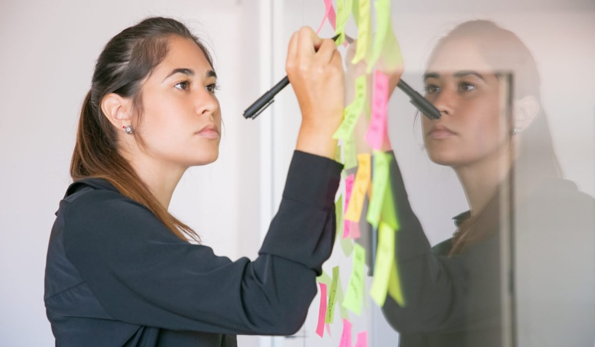 Young Latin businesswoman writing on sticker with marker. Focused confident beautiful brunette female manager sharing idea for project and making note. Brainstorming, business and training concept